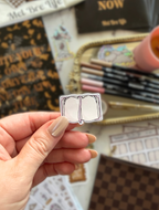 Close-up of a Pink Reading Trackers sticker featuring an open book with a pink ribbon bookmark